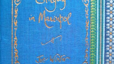 A sample cover of the book: sky-blue handloom sari with gold embossed nameplate and lettering for the title and author's name. The border of the sari lines the right hand margin of the cover.