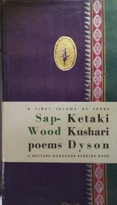 A sample cover of the book: purple handloom sari with gold embossed insignia (top centre) and the author's name and title printed on a paper strip that wraps around the lower half. The border of the sari lines the right hand margin of the cover.