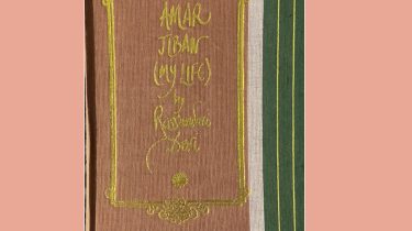 A sample cover of the book: salmon coloured handloom sari with gold embossed nameplate and lettering for the title and author's name. The border of the sari (dark green in colour) lines the right hand margin of the cover. The book is placed against a pink background.