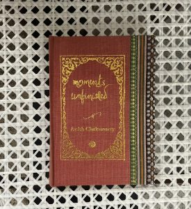 A sample cover of the book: salmon coloured handloom sari with gold embossed nameplate and lettering for the title and author's name. The border of the sari lines the right hand margin of the cover. The pocket book is placed against a white trellis background.