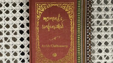 A sample cover of the book: salmon coloured handloom sari with gold embossed nameplate and lettering for the title and author's name. The border of the sari lines the right hand margin of the cover. The pocket book is placed against a white trellis background.